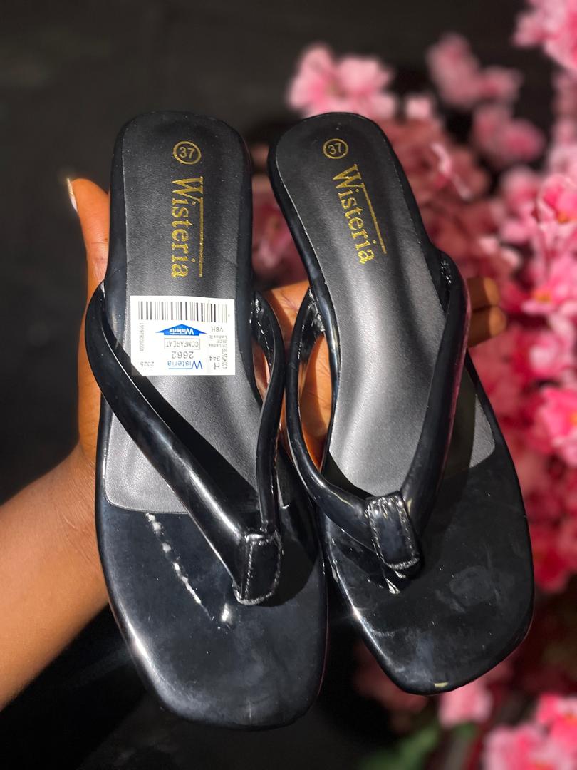 Black sandals with a visible brand label held against a blurred floral background